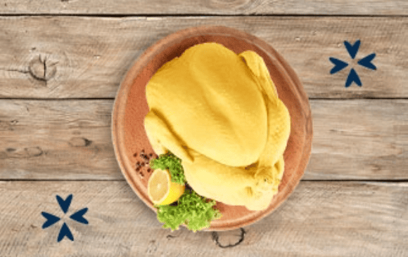 Pollo procesado sobre una tabla de madera acompañado de un limón y pimienta