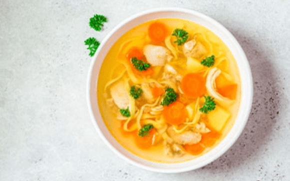Caldo de pollo con zanahorias, verduras, hierbas de olor y pollo con calidad Avigrupo servido en la mesa